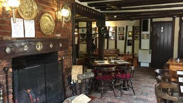 A traditional pub with exposed brick walls, a fireplace, wooden furniture, and a patterned carpet.