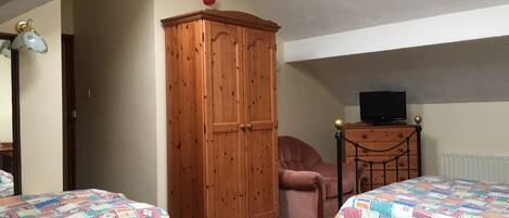 A bedroom with two beds, a wooden wardrobe, a chair, a small table with a television, and a radiator.