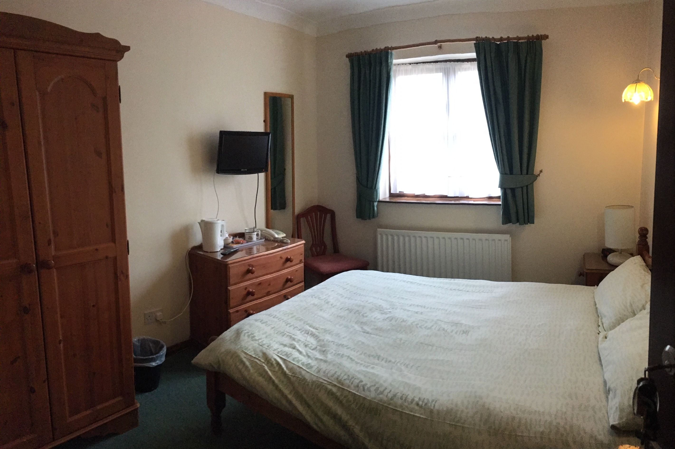 A bedroom with a bed, dresser, mirror, and a window with curtains.