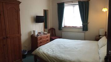 A bedroom with a bed, dresser, mirror, and a window with curtains.