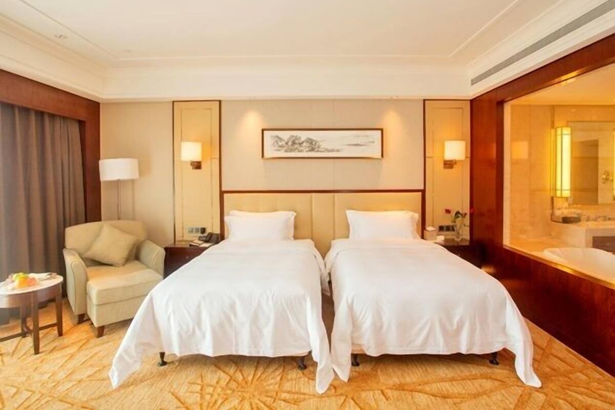 Une chambre d’hôtel avec deux lits, un canapé, une petite table avec une lampe et un tableau au mur.