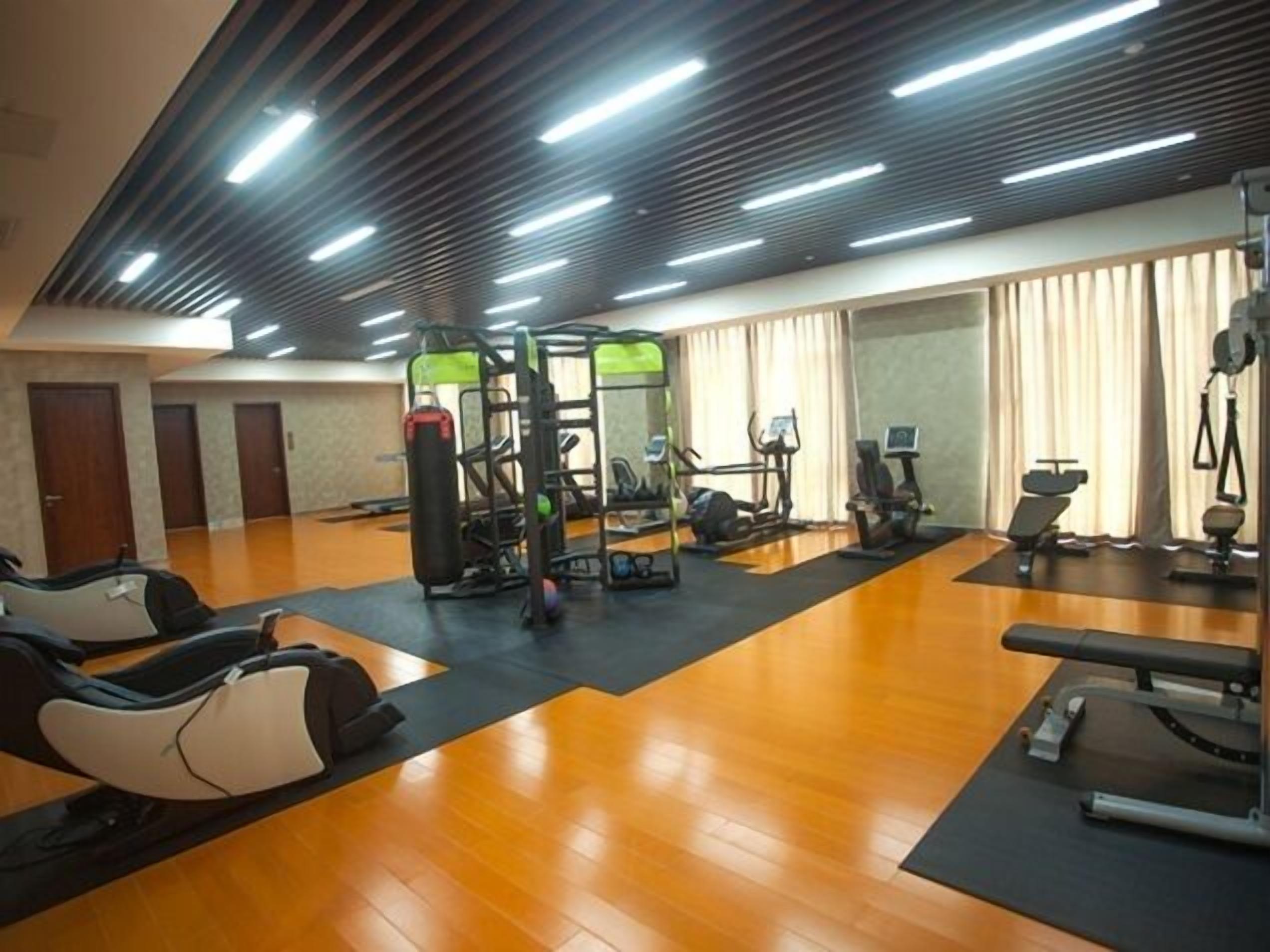 A gym with exercise equipment, wooden flooring, and a ceiling with linear lights.