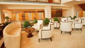 Eine geräumige Lobby mit hoher Decke, Marmorböden und einer Sitzecke mit weißen Sesseln und einem runden Tisch.