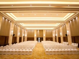 Un salón amplio con filas de sillas blancas y suelo alfombrado, que cuenta con un techo alto con iluminación empotrada.