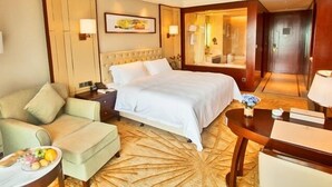 Ein Hotelzimmer mit Bett, einer Couch, einem Esstisch und einem kleinen Tisch mit Obstschale.