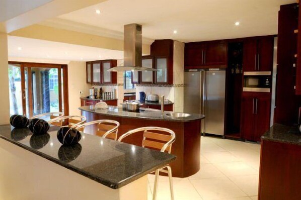 A modern kitchen with dark wooden cabinets, stainless steel appliances, and a central island with bar stools.