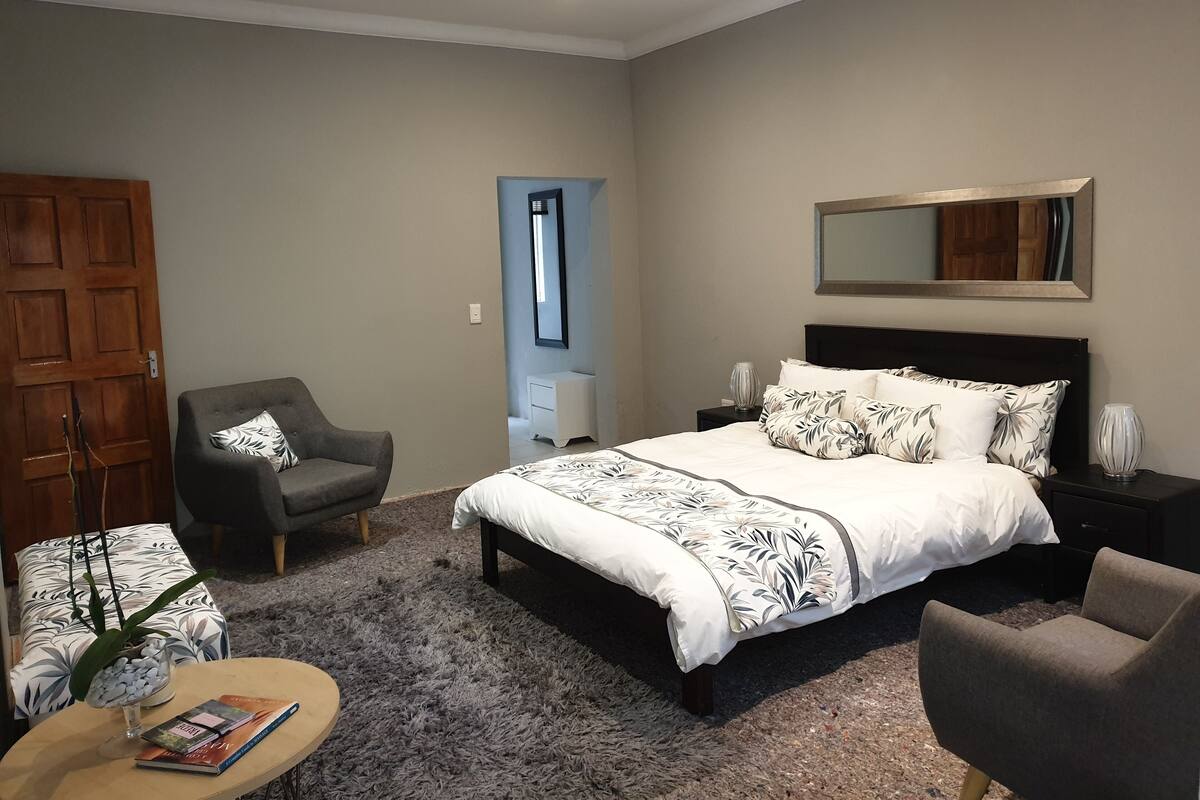 Ein Schlafzimmer mit einem großen Bett, einem Sessel, einem kleinen Tisch, einem Nachttisch und einer Tür.
