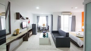 A modern hotel room with a sofa, a dining table, a TV, and a large window. - Primetime Hotel (Chonburi)