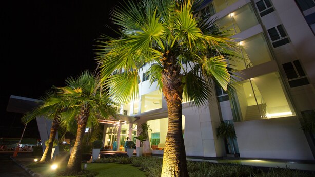 A modern building with a well-lit entrance, palm trees, and a clear view of the interior. - Primetime Hotel (Chonburi)