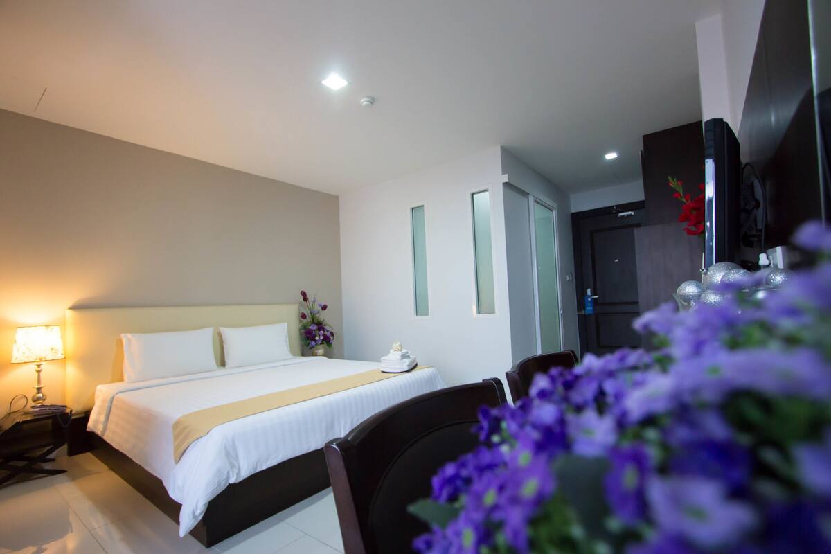A hotel room with a bed, bedside table, lamp, and a TV.