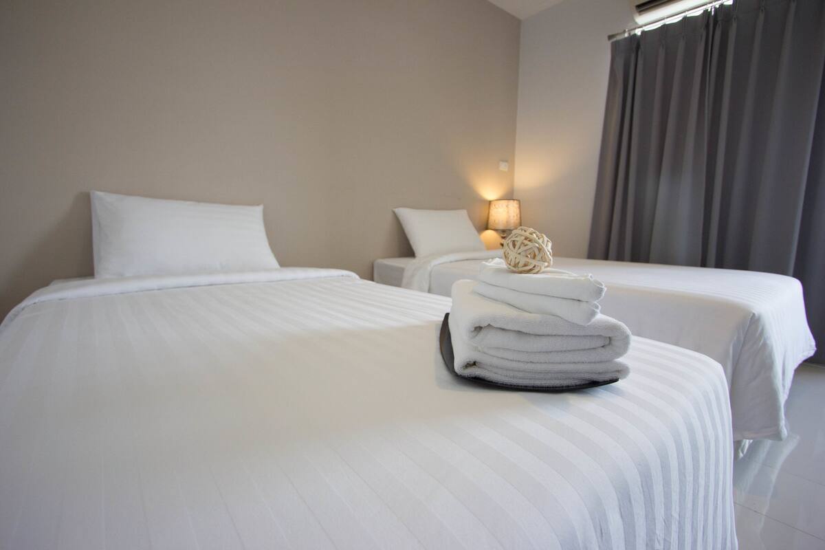 A hotel room with two beds, white linens, a lamp, and a stack of towels.