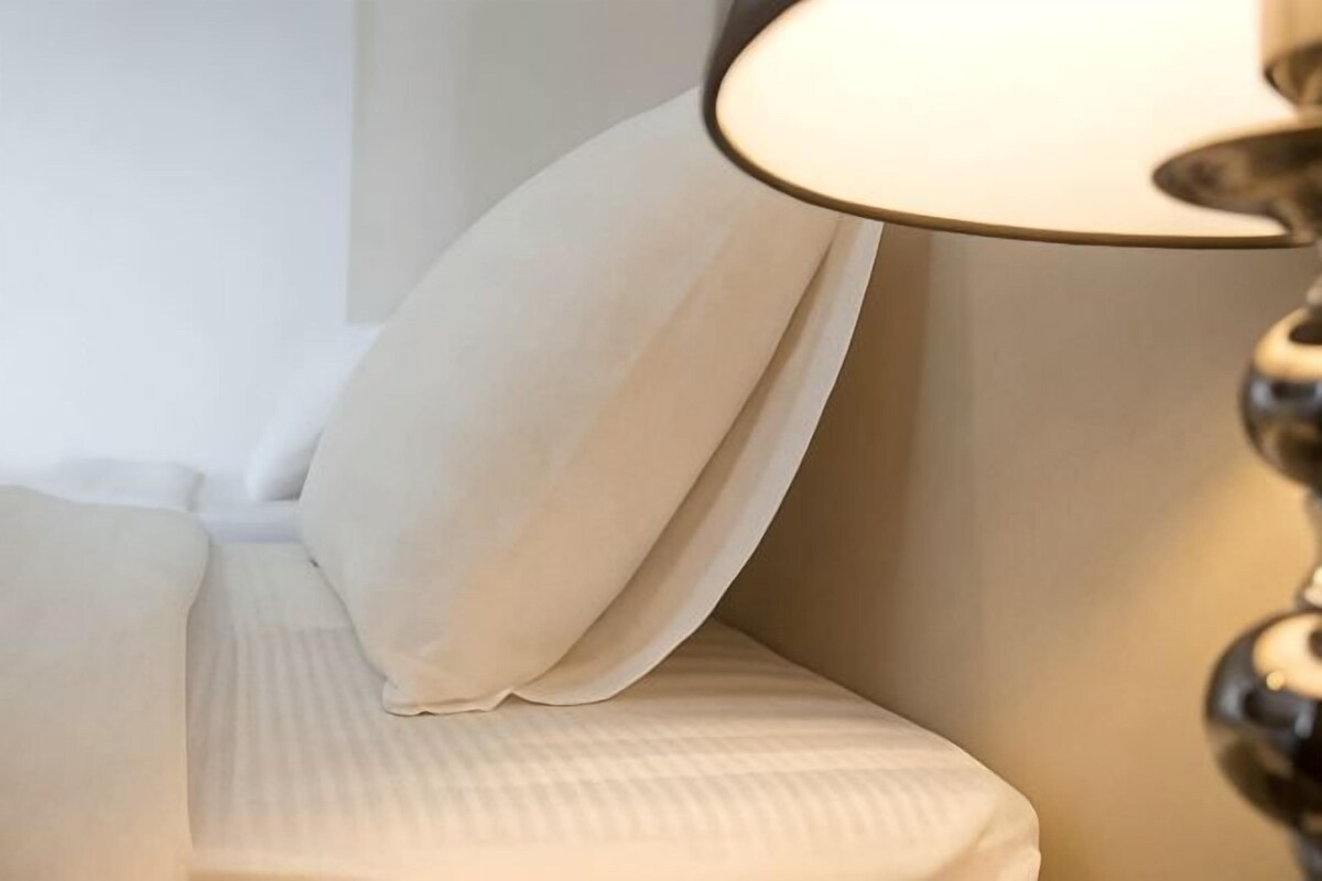 A bed with a white headboard and a lamp with a beige shade.