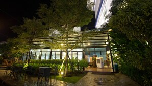 An outdoor area with a covered seating area, a building with large windows, and a well-maintained garden. - Primetime Hotel (Chonburi)