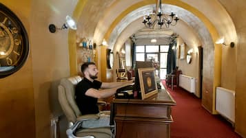 A man sitting at a desk in a hallway with arched ceilings, a clock, and a chandelier.