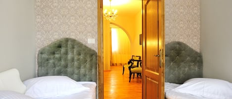Una habitación con dos camas, una araña y una puerta de madera que da a un pasillo.
