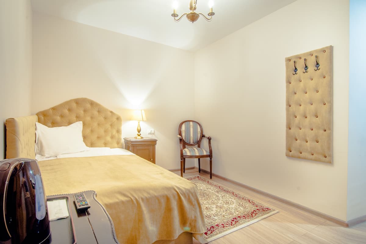 A hotel room with a large bed, a bedside table with a lamp, a chair, a wall-mounted artwork, and a coffee maker.