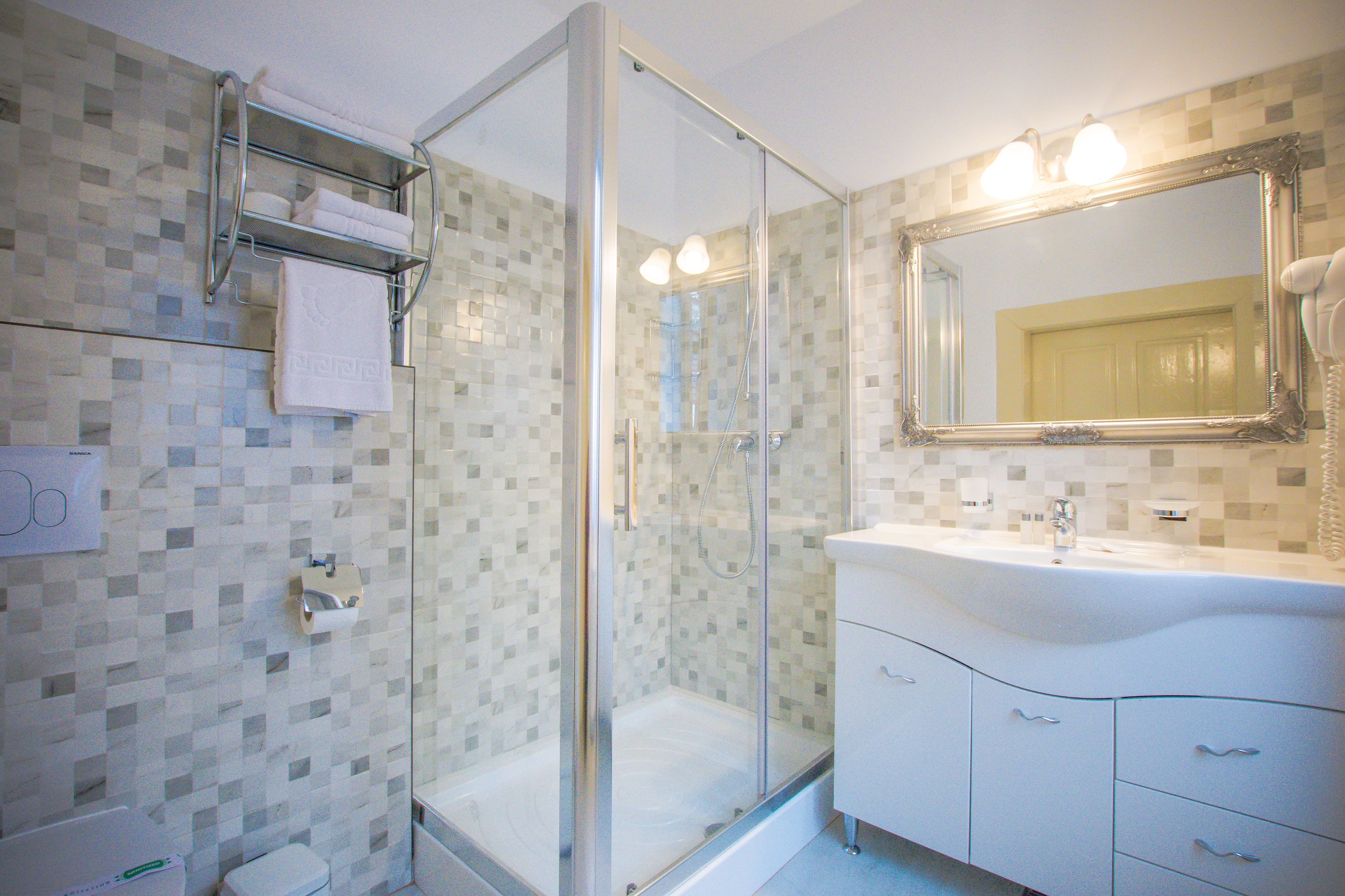 Un baño con ducha envuelta en vidrio, un lavabo blanco con espejo y pared de azulejos.
