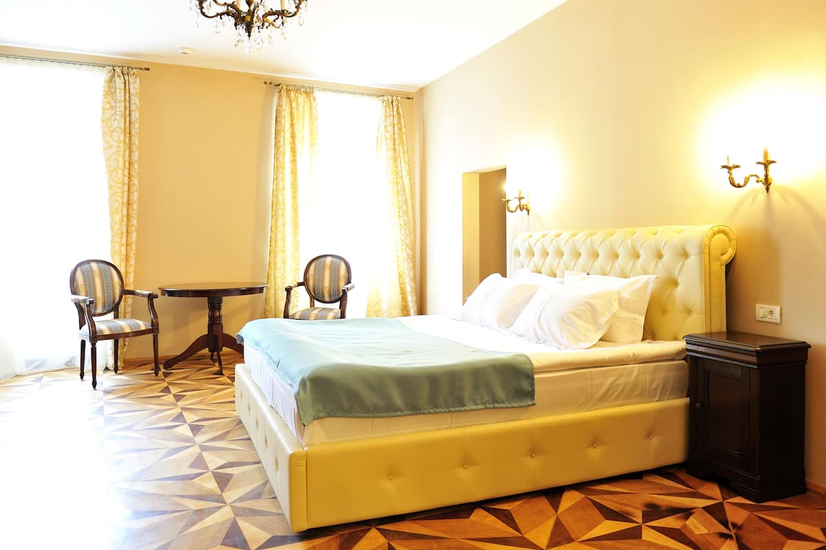 A hotel room with a large bed, a bedside table, two chairs, and a patterned floor.