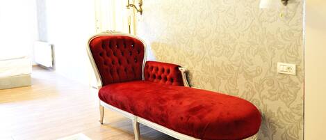 A red velvet sofa in a room with patterned wallpaper and a light fixture on the wall.