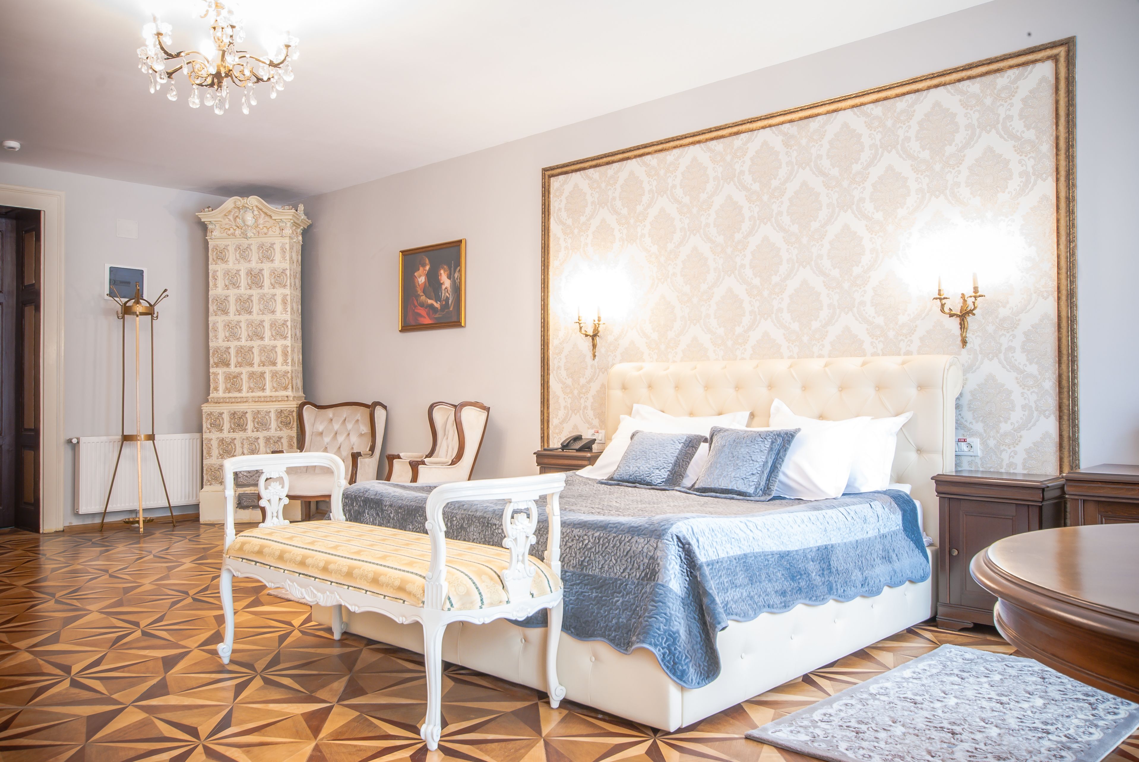 Une chambre à coucher avec un grand lit, une chaise blanche, une petite table et un lustre.