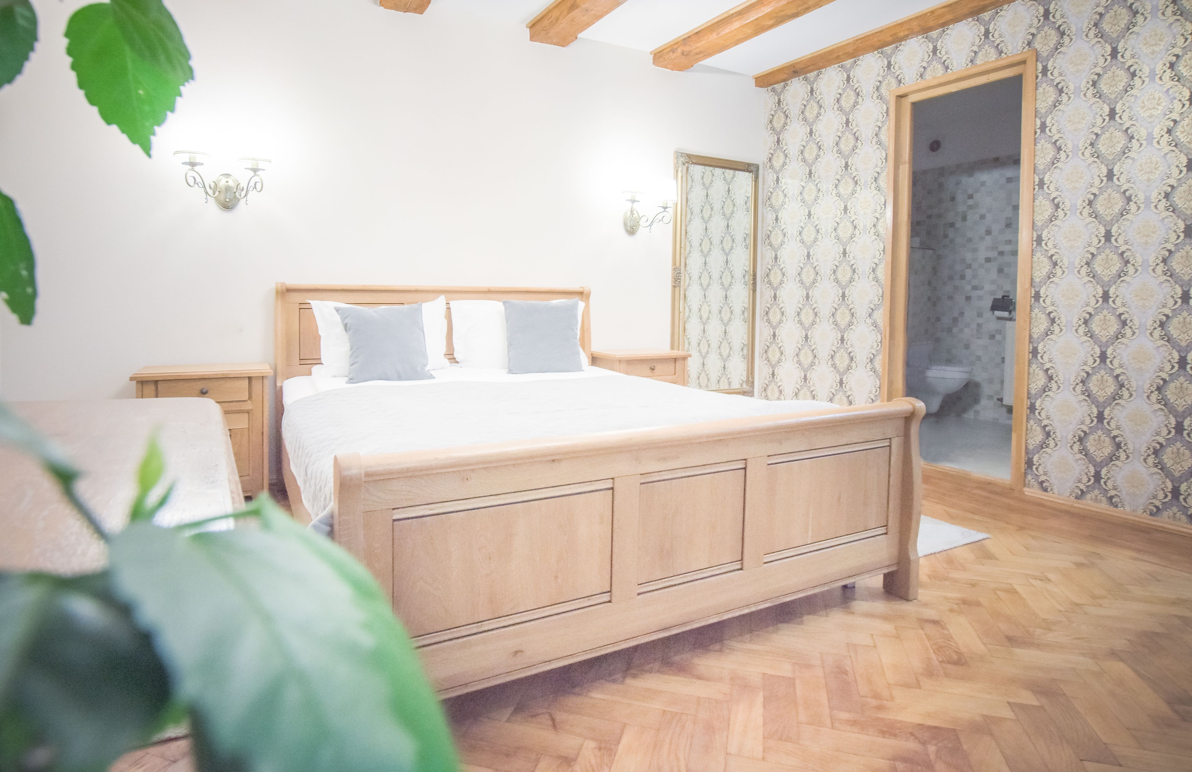 Un dormitorio con una cama de madera, una mesita de noche, una lámpara de pared y un papel tapiz estampado.