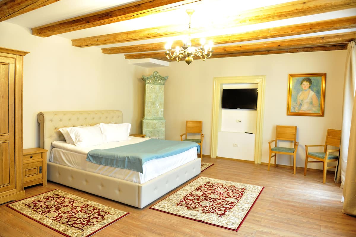 A bedroom with a bed, wooden floor, a chandelier, a dresser, a cabinet, a mirror, and two chairs.