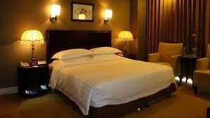 Habitación de hotel con una cama grande, dos lámparas de noche, un cuadro en la pared y una silla junto a la ventana.