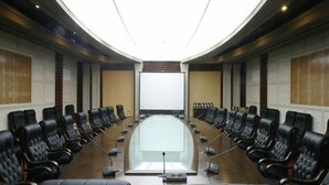Un salón de conferencias con una larga mesa, sillas de cuero negro y una gran pantalla al frente.