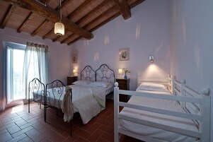 A bedroom with two beds, a wooden ceiling, a window with curtains, and wall-mounted lamps.