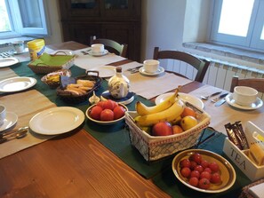 Ein Esstisch mit Geschirr, Obstschalen, einem Teekessel und einer Kaffeemaschine.