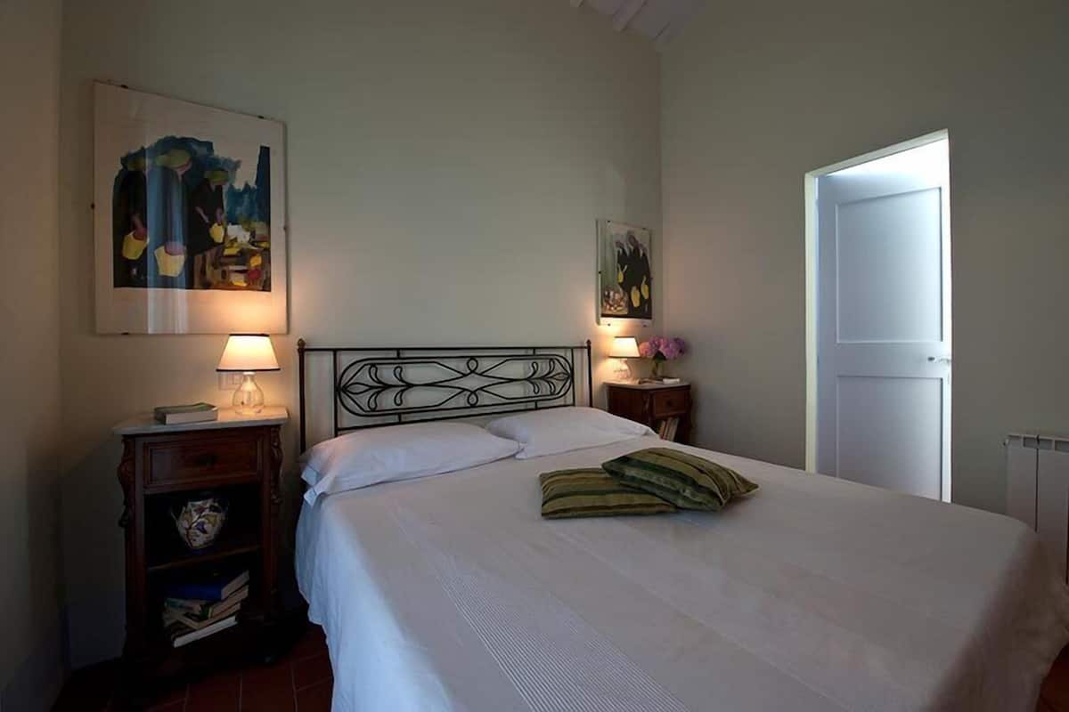 A neatly made bed with white linens, two bedside tables with lamps, and artwork on the walls.