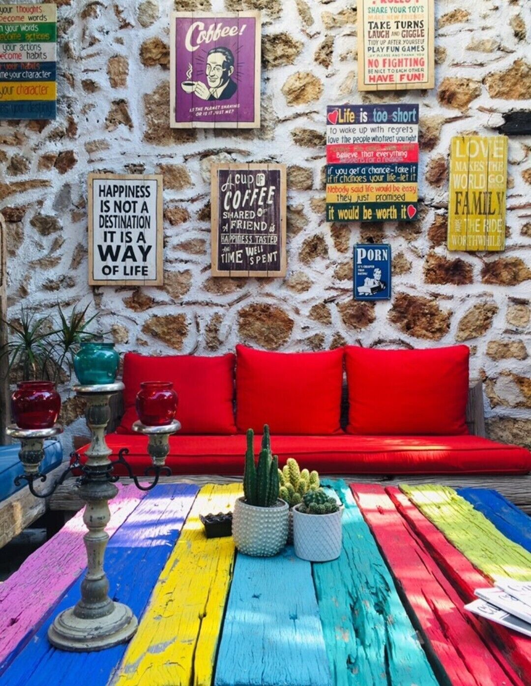 A colorful outdoor seating area with a stone wall, red cushions, and various motivational signs.