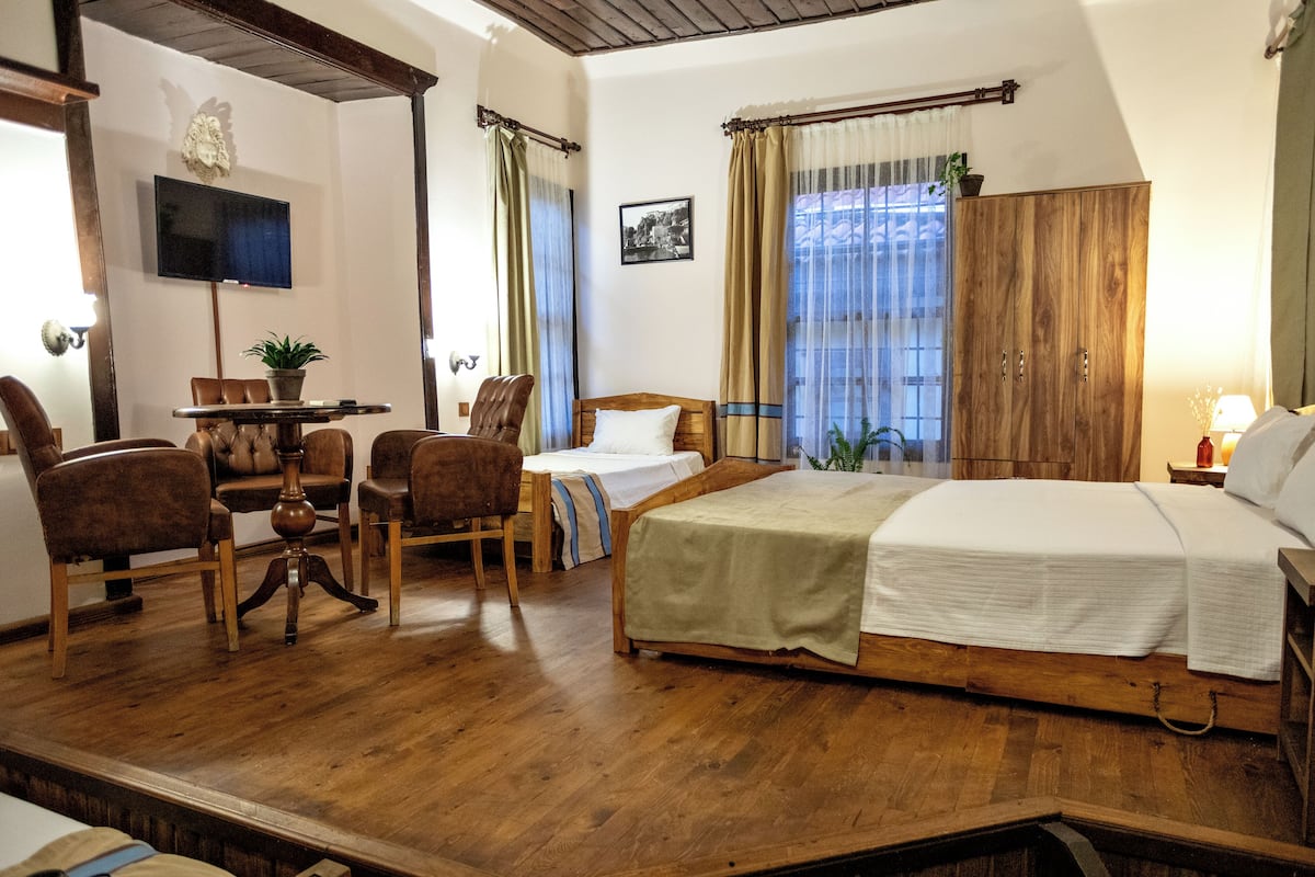 Una habitación con cama, escritorio, sillas, televisor y armario.