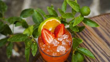 Un verre de boisson glacée aux fraises, garni d’une tranche de citron vert, entouré de feuilles vertes.