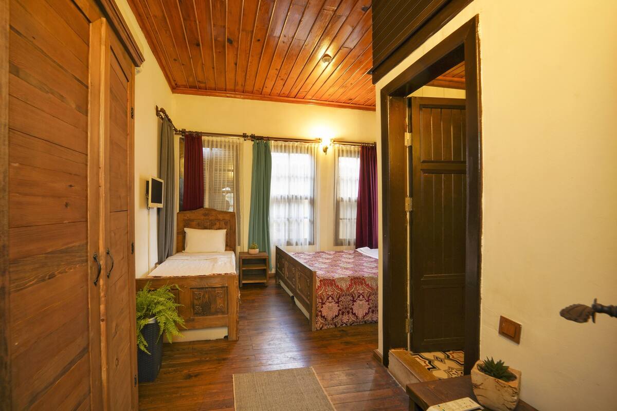Una habitación acogedora con techo de madera, dos camas con ropa de cama floral, una mesita de noche con una planta y un armario de madera.