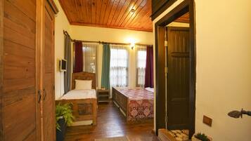 Una habitación acogedora con techo de madera, dos camas con ropa de cama floral, una mesita de noche con una planta y un armario de madera.