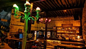 Un espace bar avec un plafond en bois rustique, un comptoir bien garni de bouteilles variées et une enseigne indiquant « VIEILLE MAISON ».