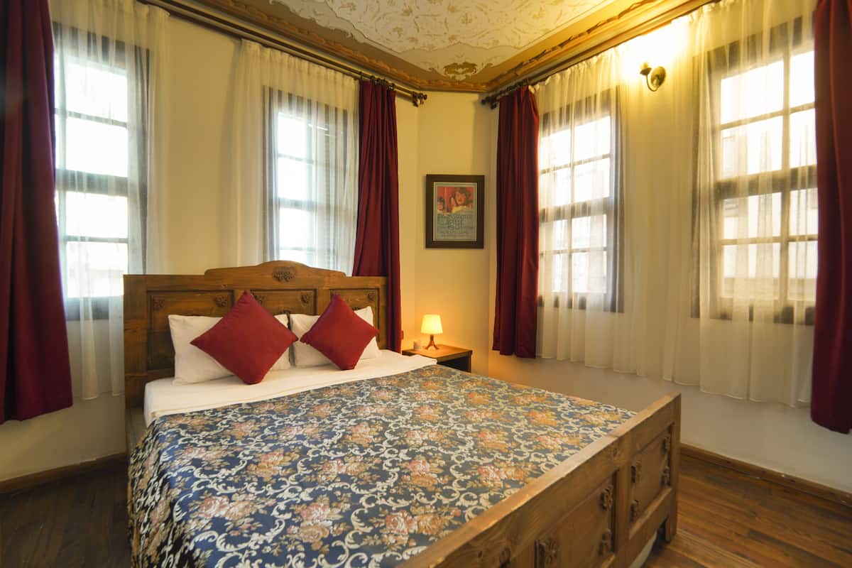Un dormitorio con una cama grande, cabecera de madera, cortinas rojas y blancas, y un cuadro enmarcado en la pared.
