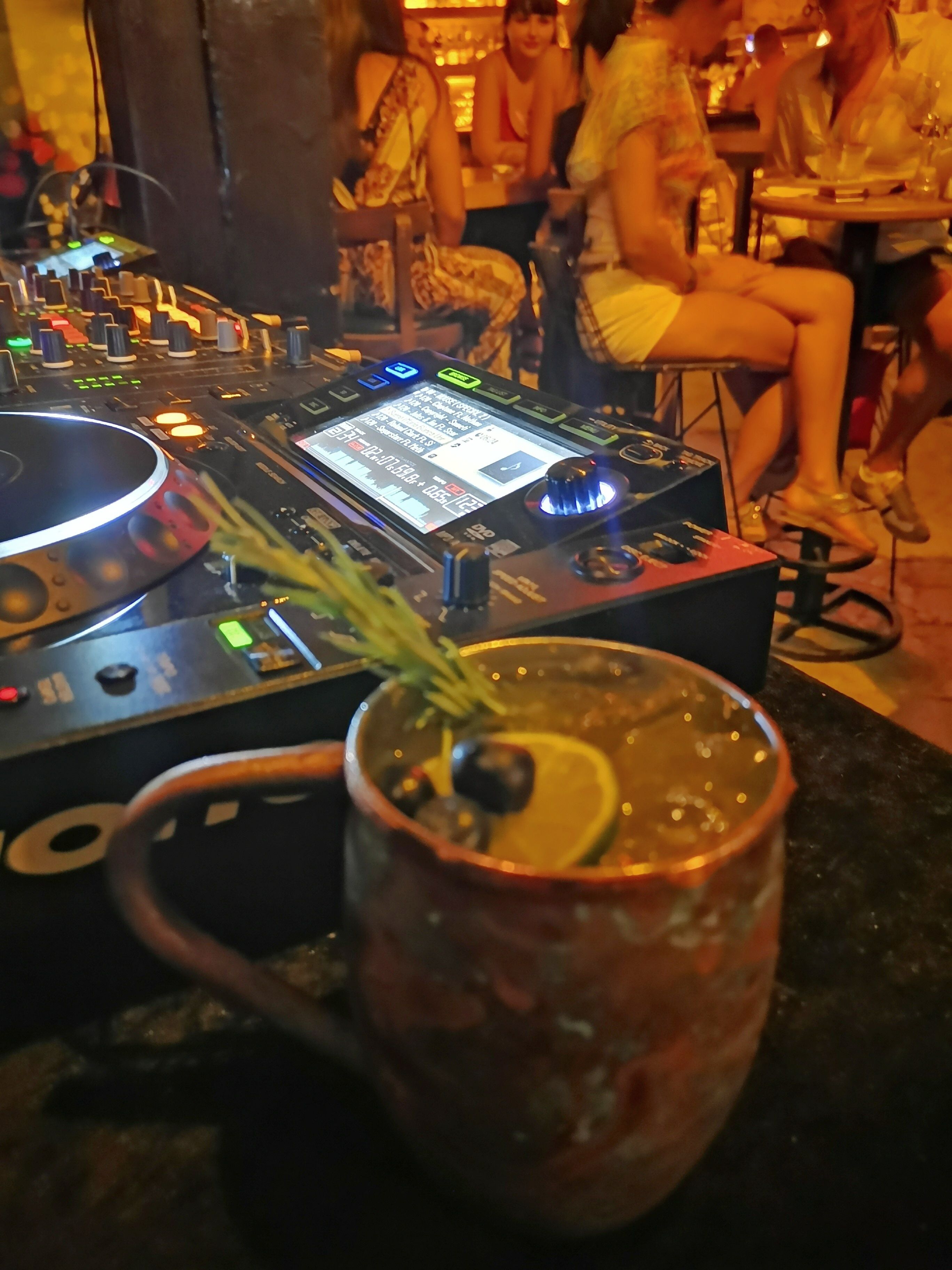 A DJ booth with a digital display and a cocktail glass with a lemon slice on a table.