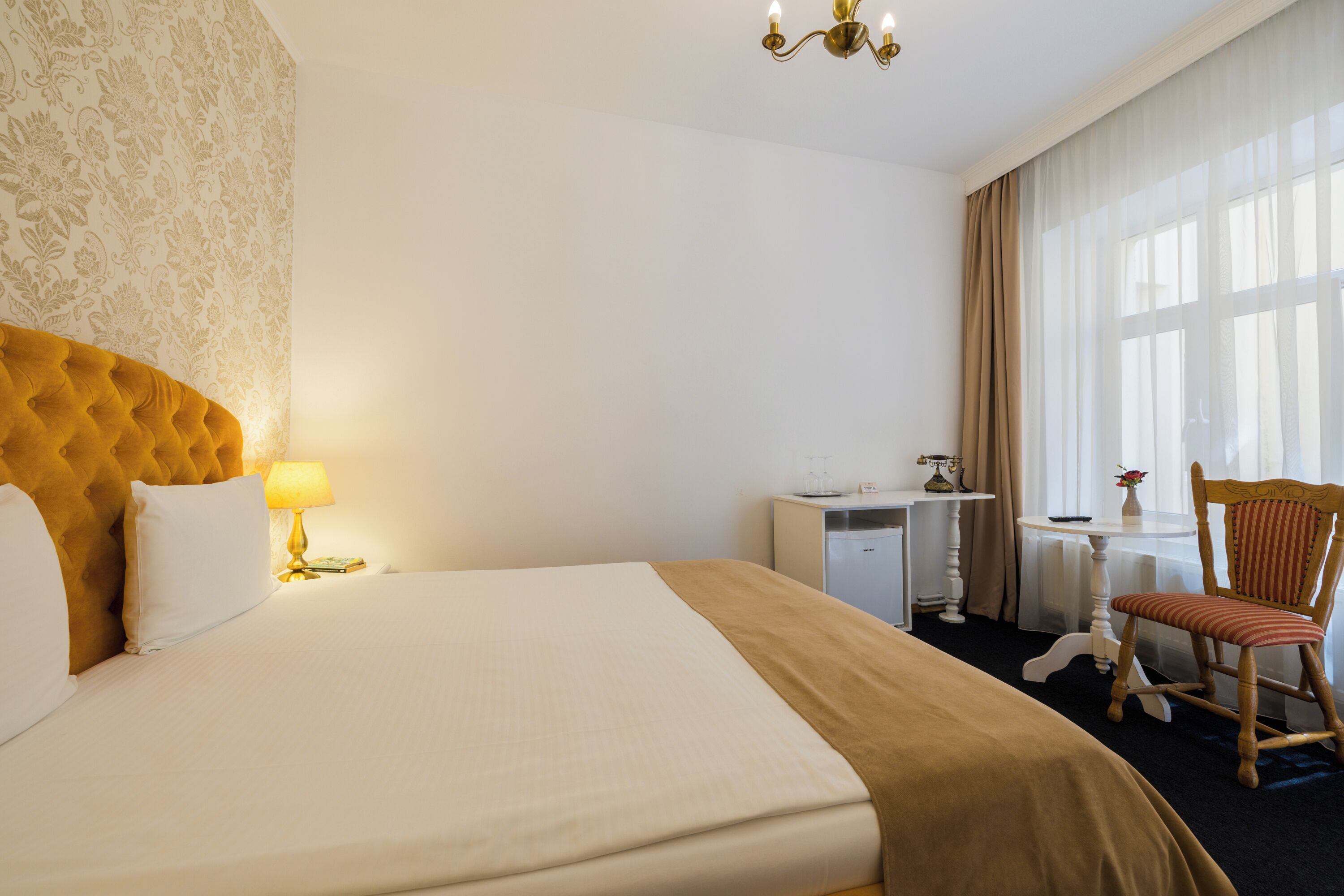 Una habitación de hotel con una cama grande, un escritorio, una silla y un ventanal con cortinas.