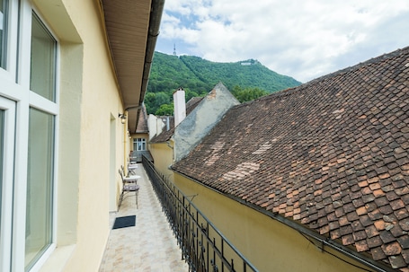 A narrow alleyway with a tiled roof, a balcony with outdoor furniture, and a mountain in the background.