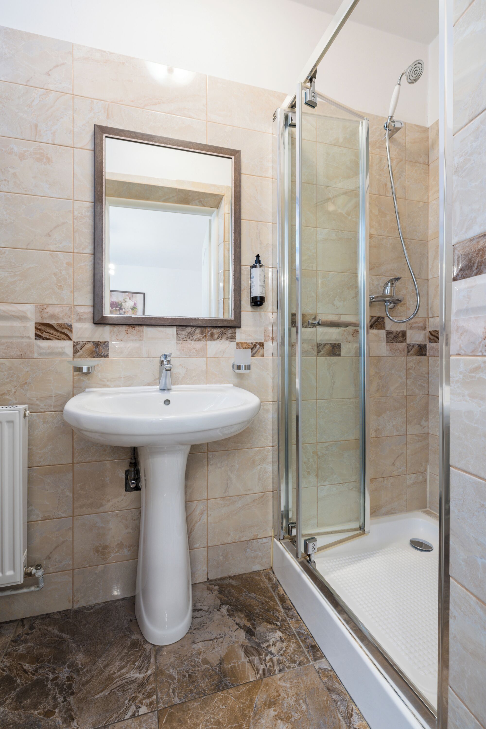 A bathroom with a pedestal sink, a glass-enclosed shower, and a mirror above the sink.