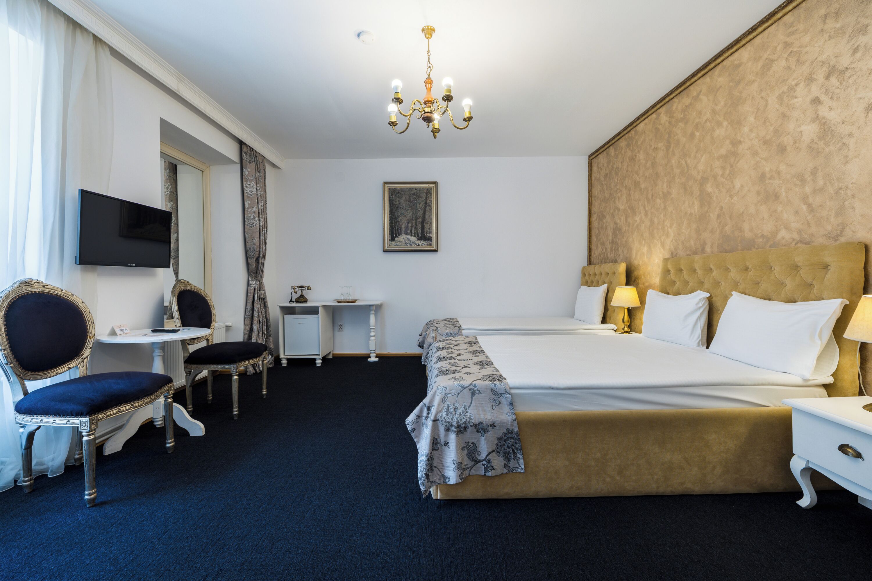 Camera d'albergo con un letto grande, due comodini con lampade, una TV a parete, un tavolino con una sedia e un lampadario.