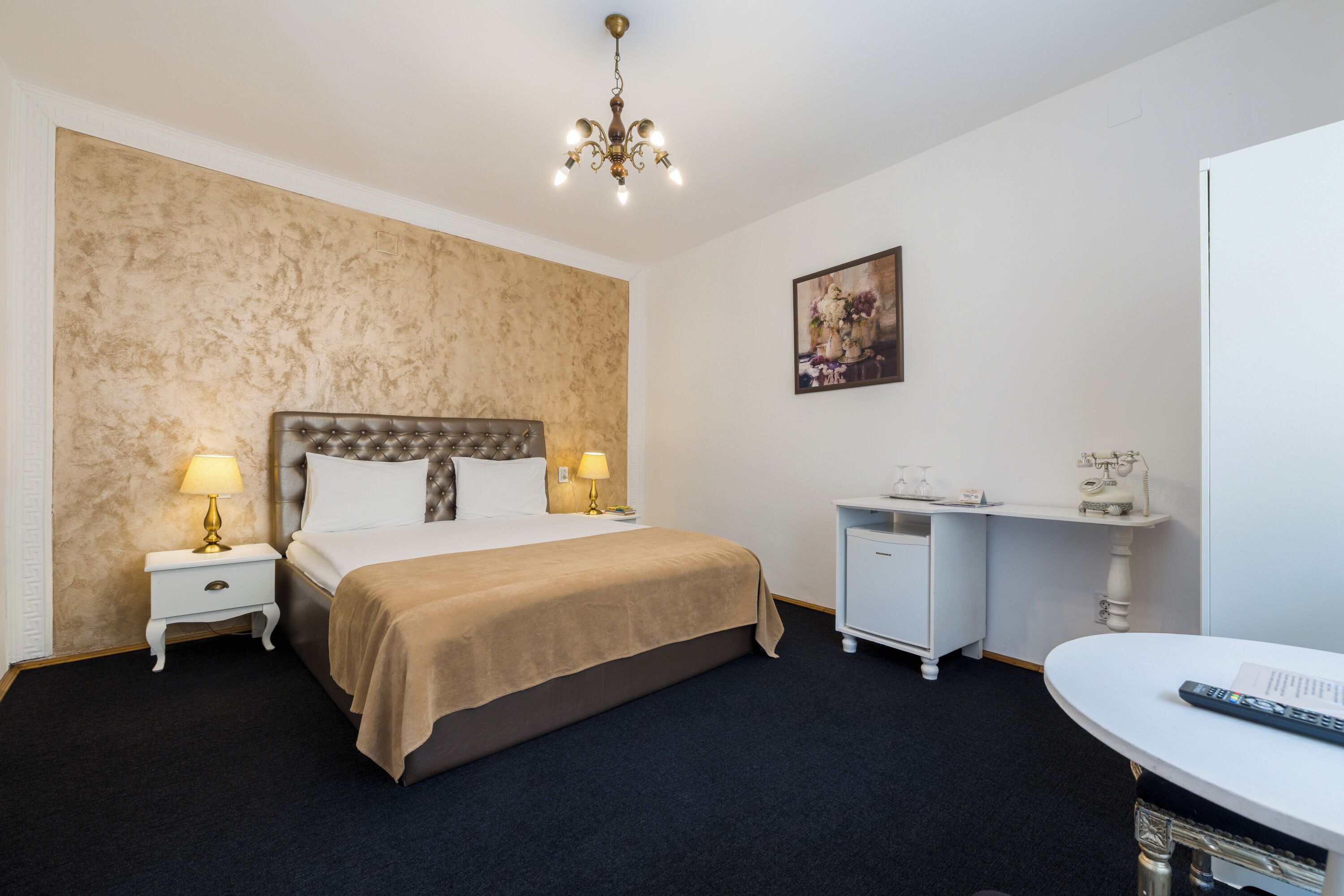 A hotel room with a large bed, two bedside tables with lamps, a desk with a chair, and a painting on the wall.