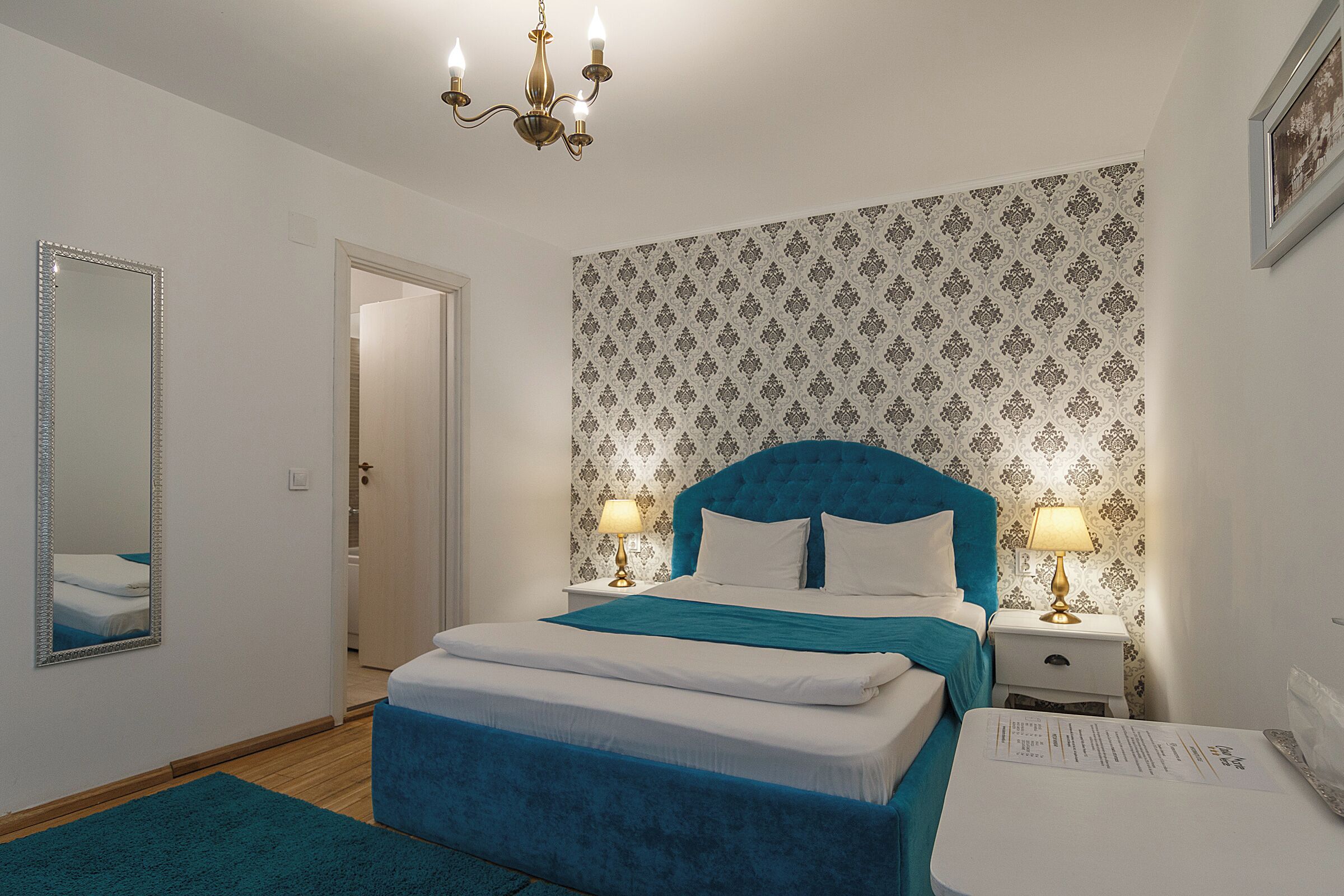 A bedroom with a bed, bedside tables, a mirror, and a chandelier.