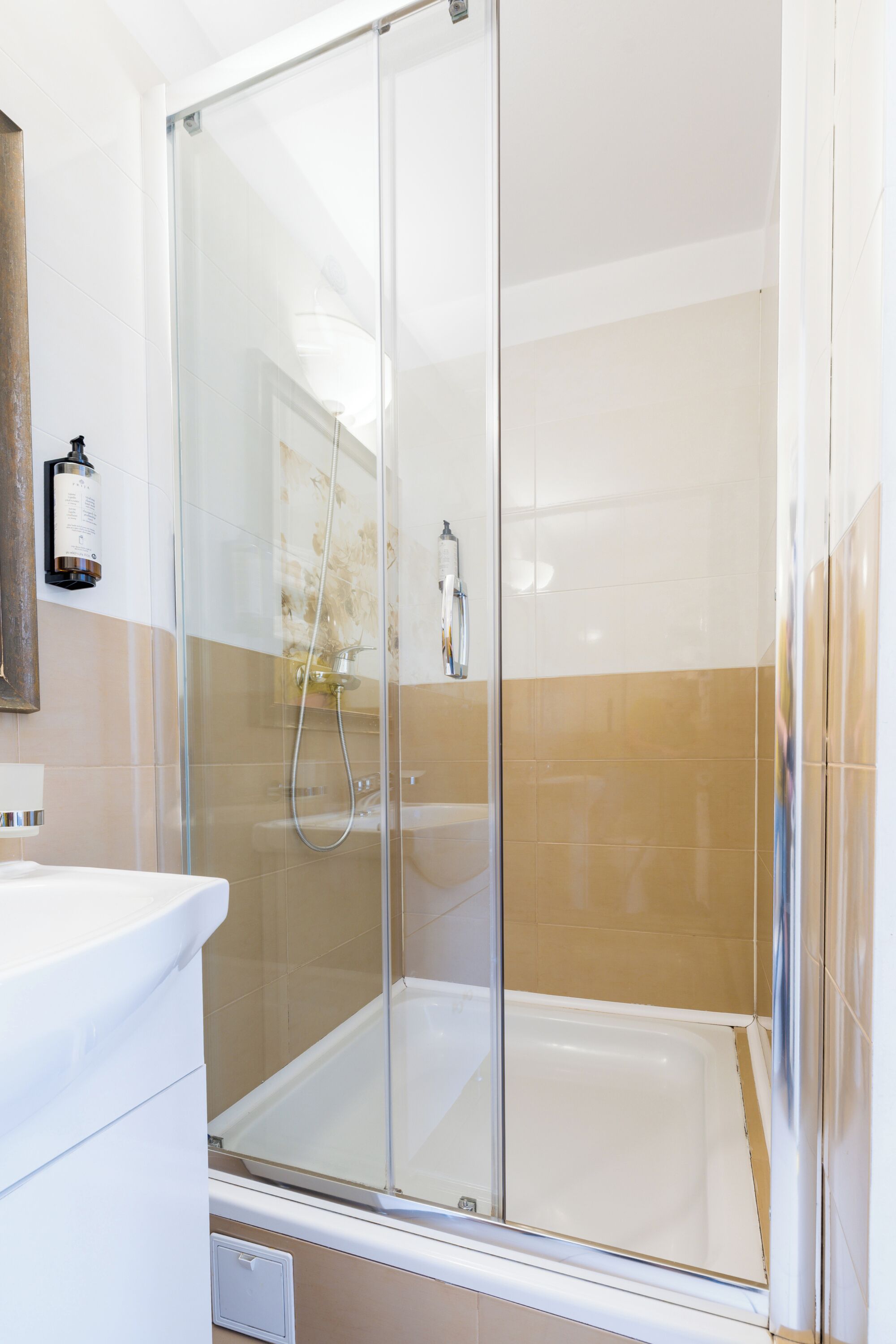 Ein modernes Badezimmer mit einer Duschkabine aus Glas, einem weißen Waschbecken und beigen Fliesen.