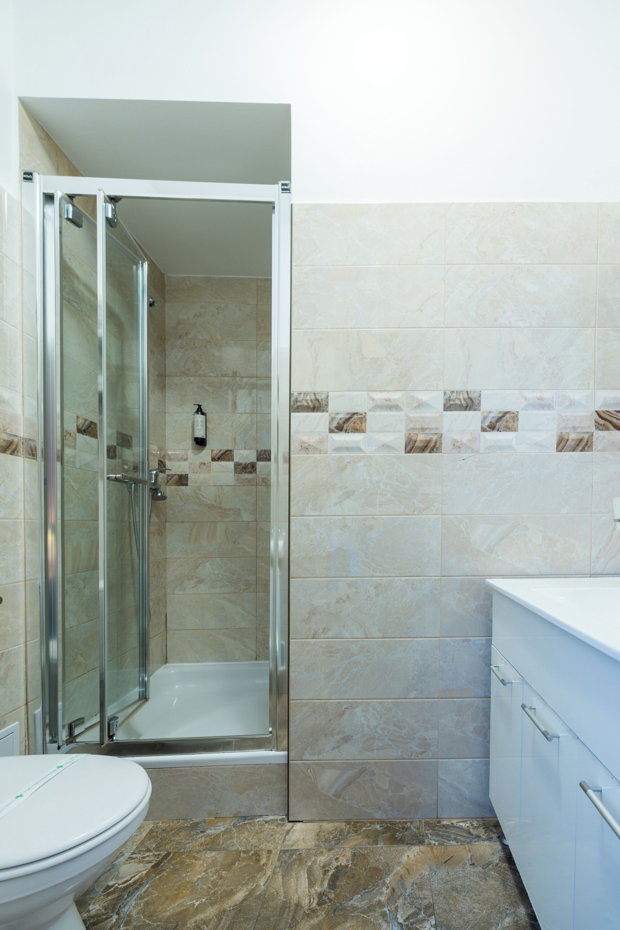 A bathroom with a glass-enclosed shower, a white toilet, and a white sink with a cabinet.