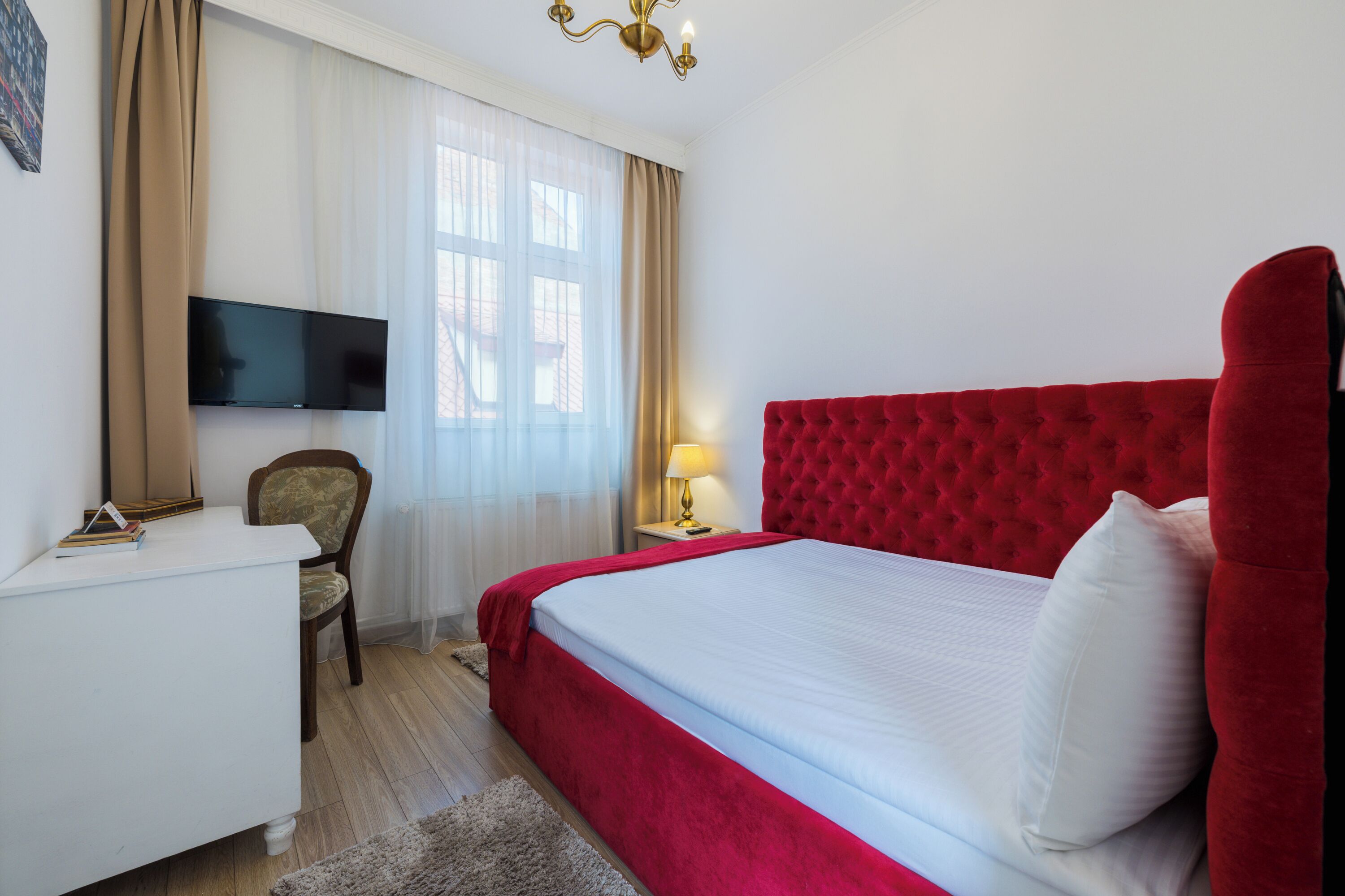 Hotellihuone, jossa on suuri sänky, seinälle asennettu televisio, työpöytä ja tuoli.