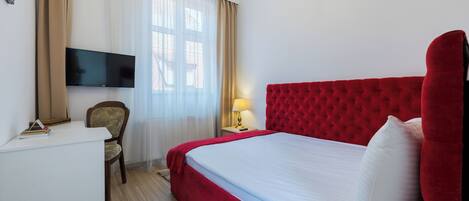 Una habitación de hotel con una cama grande, un televisor en la pared, un escritorio y una silla.