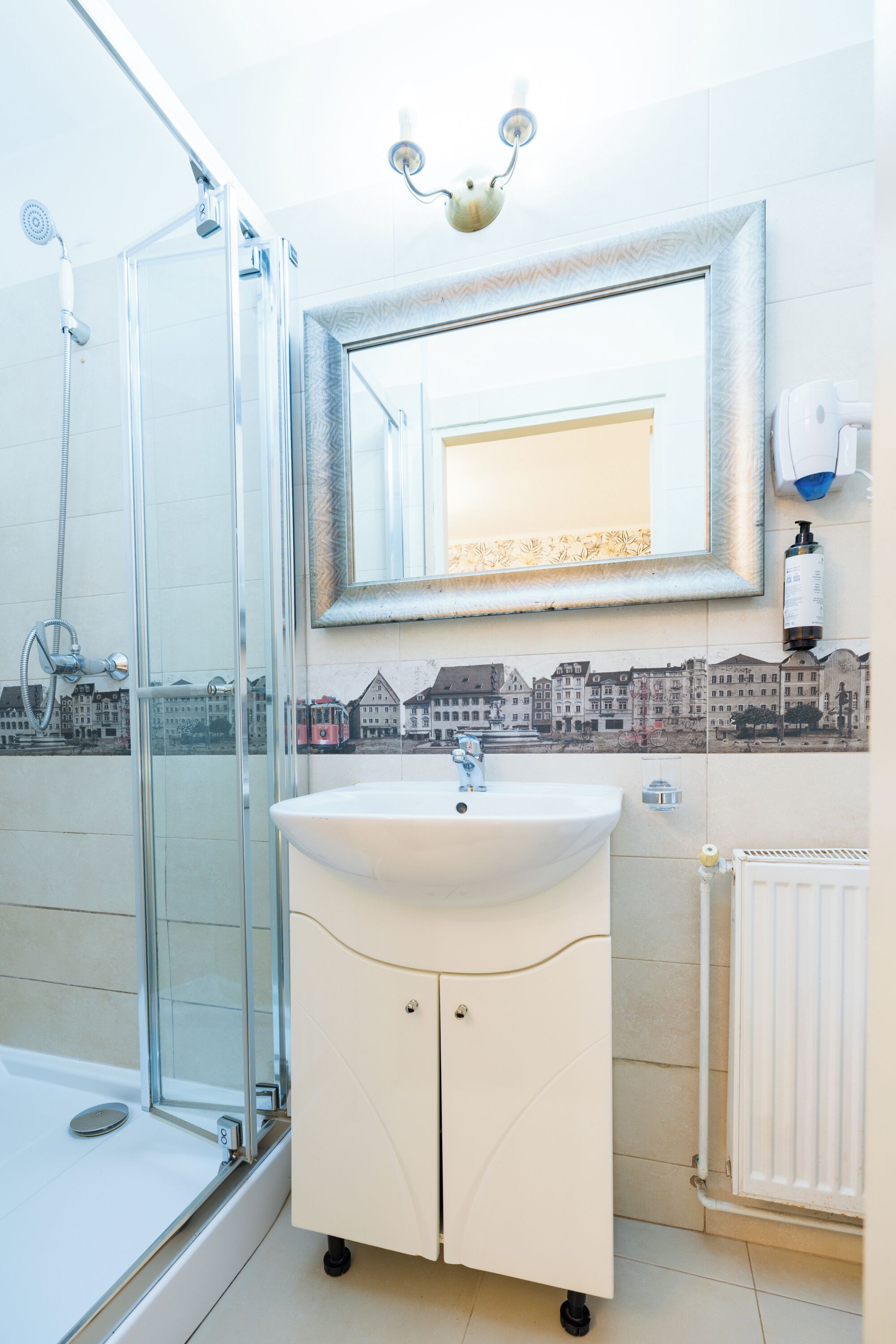 A bathroom with a glass shower enclosure, a white sink with a mirror above it, and a radiator on the wall.